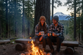 Two people by campfire holding Pacific Northwest mugs