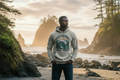 Athletic diverse male model wearing the Pacific Northwest Beach Hoodie on a rocky coastline at golden hour